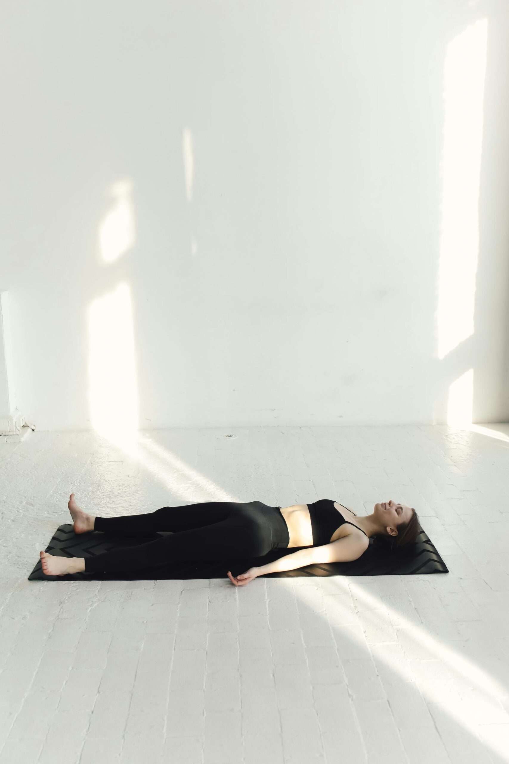 Yoga practice session with a woman relaxing on a mat in a bright, sunlit room.